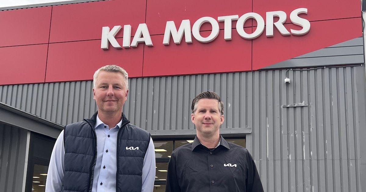 två leende män framför en fasad med texten KIA Motors