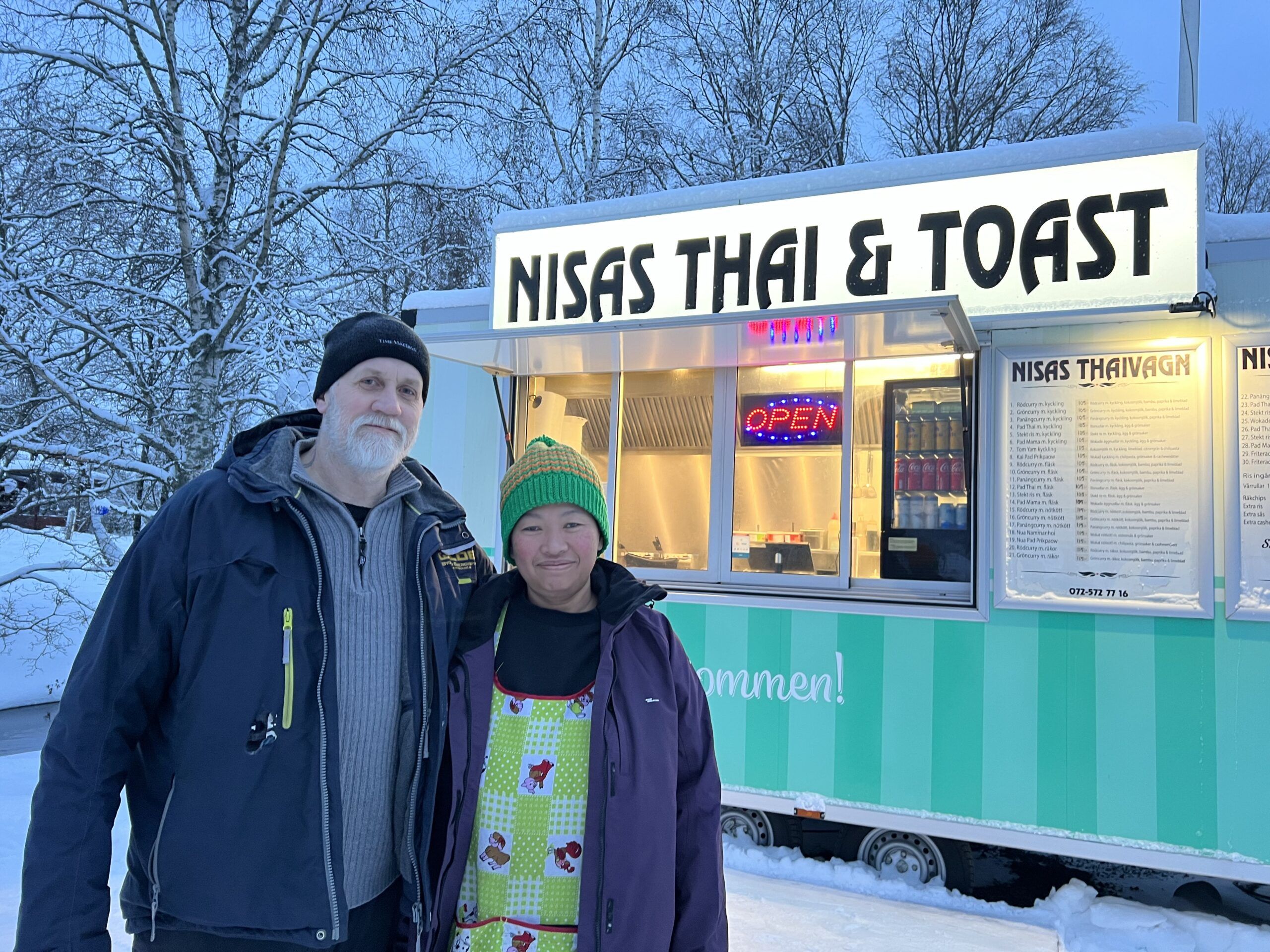 en man och en kvinna i vintermiljö framför en upplyst matvagn